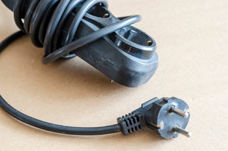 Old black extension cord on the floor close-up. Power extension cord wrapped around. Electrical...