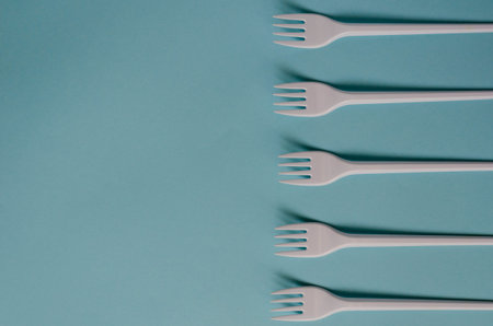 Abstract background with disposable cutlery. Plastic forks on a light blue background. A group of...