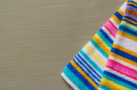 Multi-colored striped beach towel close-up. Colorful rainbow colored towel on a light brown textured...
