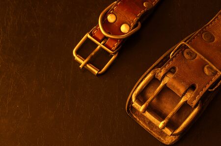 Fragment of two old genuine leather collars on a dark table. Cracked shabby leather and metal fittings. Real vintage dog collars. Love to the animals. Selective focus.の写真素材