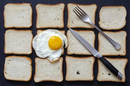Creative background with fried egg and toast bread. A single fried chicken egg with a fork and knife on a background of pieces of bread. Breakfast at the roadside cafe. Traveling by car, tourism.の写真素材
