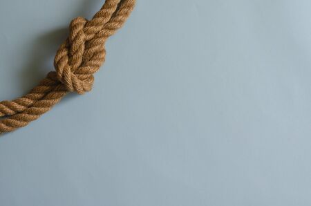 Hemp rope with a nautical knot on a light blue background. Knotted natural rope. Multitask background for design tasks. Place for text.の写真素材