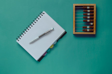 Creative turquoise background with wooden abacus, notebook and pen. Warehouse accounting or...