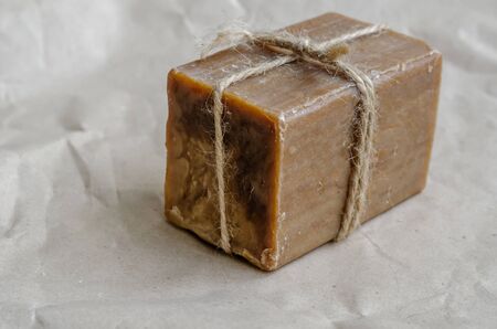 A piece of laundry soap on a plain background. A single rectangular piece of new soap wrapped with twine. Natural hygiene products. Place for text. Selective focus.の写真素材
