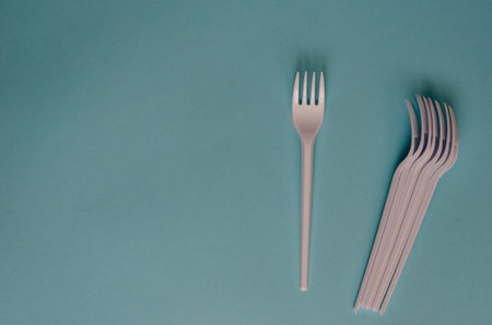 White plastic forks with shadows on a light blue background. Creative background using disposable...