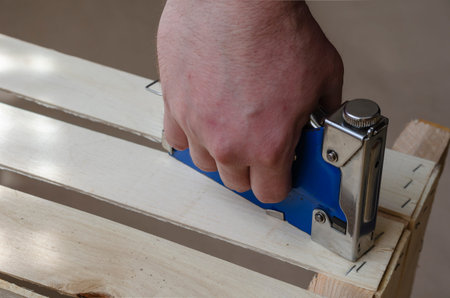 A man collects a wooden box using a stapler. Production of eco-friendly wooden containers for packaging, storage and transportation of vegetables and fruits. Industrial topics. Selective focus. Copy space.の写真素材