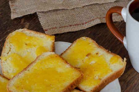 Slices of bread with linden honey on a dark wooden background. Plate with sweet sandwiches. A cup of...