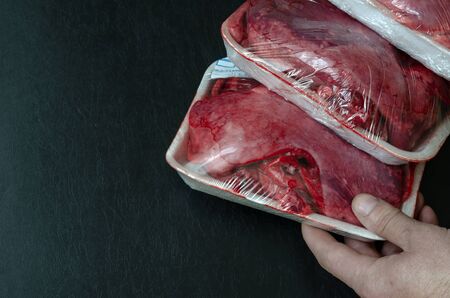 The buyer chooses a tray of raw beef lungs. A male hand holds a packaged serving of raw offal. Top view at an angle. Copy space. Selective focus.の写真素材