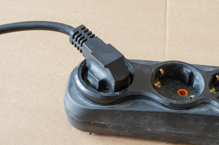 Used electric extension cord on a beige background. Black developer with a plug in the plug....