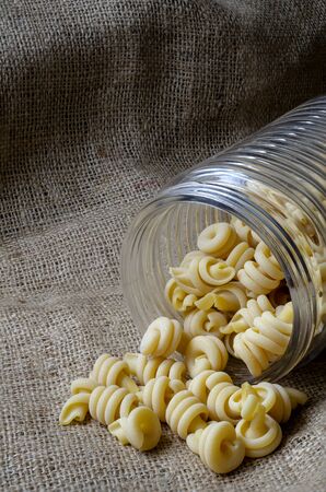 Uncooked insalatonde pasta in a glass jar on burlap. Traditional Mediterranean cuisine. Gastronomy. Copy space. Close-up.の写真素材