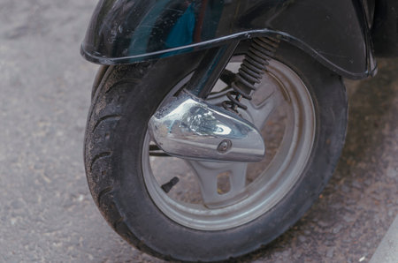 Wheel of a modern moped or minibike in a street parking lot. Closeup of a wheel with dirt and dust....