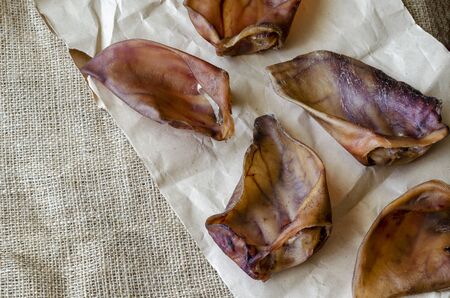 Five dried pork ears on burlap. Dental treats for cleaning teeth from pet plaque. Pet supplies.の写真素材