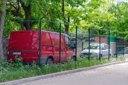 Nikolaev, Ukraine - May 31, 2020: parking fenced with metal mesh on the front lawn. Red minibus and...