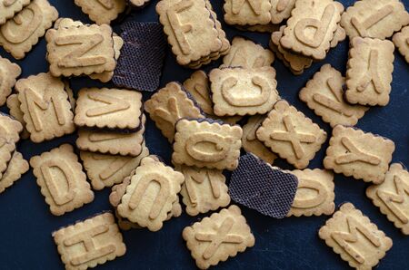 Cookies alphabet close-up. A pile of biscuits with English letters background. Rectangular tasty cookies with a chocolate base.の写真素材