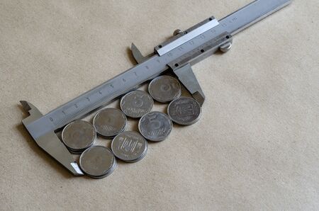 Light coins and vernier caliper. The caliper measures Ukrainian coins of a face value of 5 kopecks. Light coins of the same denomination. Bankrupt, poverty. Close-up. Selective focus.の写真素材
