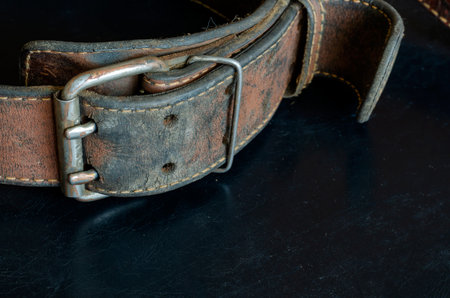 Cracked very old leather belt with a double metal buckle. Close-up of a wide dirty belt or collar on...