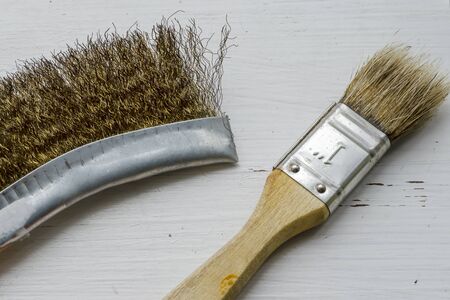 Paint brush and metal brush on a white wooden background. Cracked white paint. Commercial painting services. Close-up. Selective focus.の写真素材