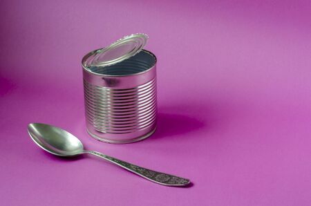 Empty tin can and spoon on a purple background. Tin can and metal spoon. Canned food. Close-up. Copy space.の写真素材