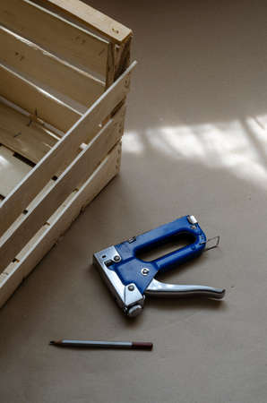 Blue industrial stapler, pencil and wooden box in the sunshine indoors. Production of environmentally friendly packaging for the transport of food. Top view at an angle. Selective focus.の写真素材