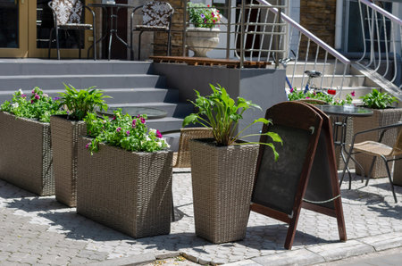 Summer street cafe without anyone.Empty tables of a street coffee shop. Wicker baskets with ornamental plants zone the space. Summer sunny day. Travel, tourism. Selective focusの写真素材
