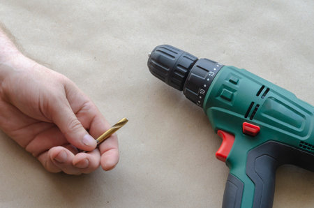 Man's hand holds a broken drill for metal. An electric drill lies nearby. Inept Use of a hand-held...