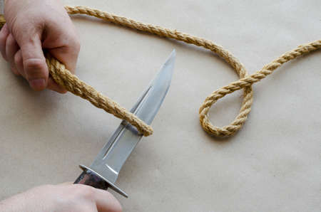 Hands of an adult cut a hemp rope with knife. Man of Caucasian ethnicity, aged 44-45 years. Top view at an angle. Selective focus.の写真素材