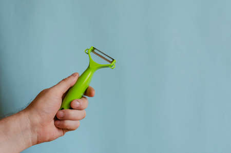Hand holds a knife for peeling vegetables. Left hand of a man with a green kitchen knife. Caucasian man 43-45 years old. Kitchenwareの写真素材