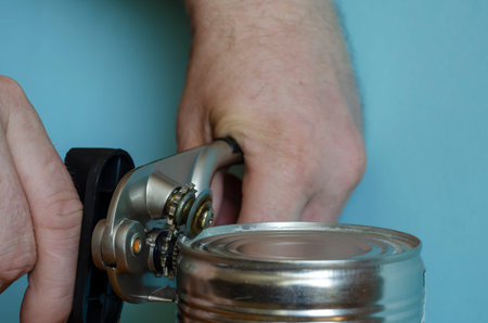 Hands of a man opens a tin can with a can key. Closeup of the process of opening canned food. Adult...
