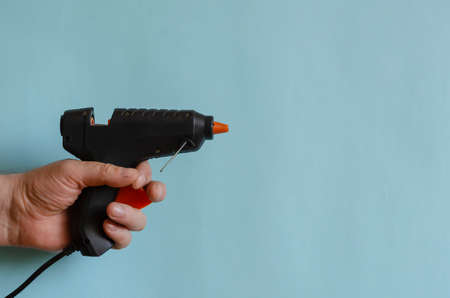 Glue thermo gun in a male hand. An electric device for gluing objects with sticks of glue. Middle-aged man of European race. Hand-held power tools for work and creativityの写真素材