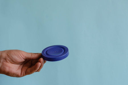 Hand holds a blue plastic lid for a can. The left hand of a person with a food plastic product...