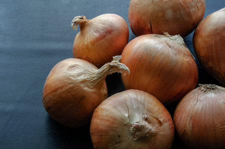 Brown raw onions in a peel on a dark table. Close-up of a farm crop from the garden. Organic...