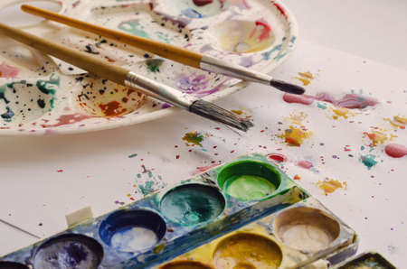 Artistic brushes, set of paints on splattered watercolor table. Creativity, hobbies, education. Side view at an angle. Selective focus.の写真素材