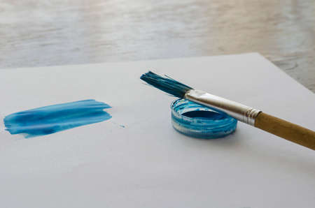 Art brush and brushstroke of blue watercolor paint on white paper. Drawing lessons. Training, hobbies, education. Top view at an angle. Selective focus.の写真素材