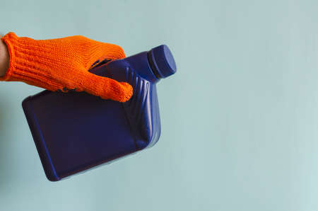 Full blue canister in a man's hand. Man's hand in a protective glove holds a plastic can of liquid. Male European race. Car service, auto products.の写真素材