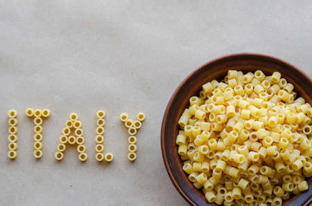 Word Italy from capital English letters is laid out with dry paste of Ditalini. Clay Bowl with pasta nearby. Varieties of Mediterranean food. View from above.の写真素材