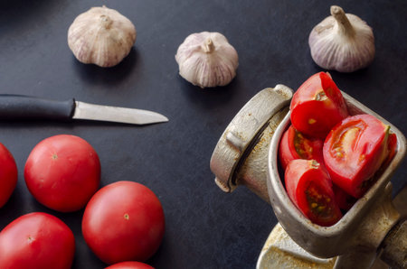 Manual vintage meat grinder and ripe vegetables on the table. Red tomatoes and a head of garlic....