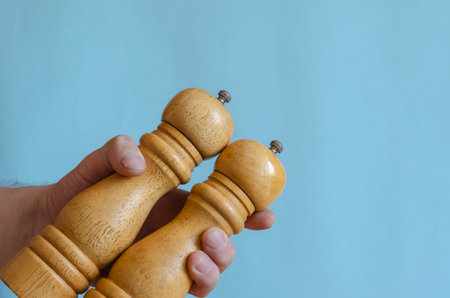 Adult man holds in his hand two wooden pepper mills. Devices for grinding spices from hard wood....