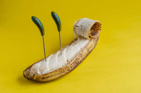 Overripe banana with partially peeled skin and canape skewers. Sliced sweet fruit on yellow background. Side view. Selective focus.の写真素材