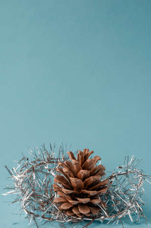 Pine cone and Christmas tree tinsel on light turquoise background. Celebrating Christmas and New Year.の写真素材