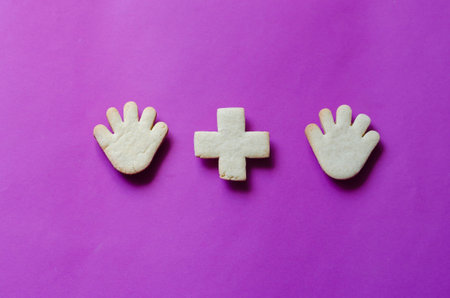 Homemade curly shortbread cookies. Figures of hands and arithmetic plus sign on a purple background....