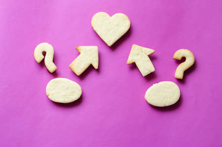 Creative background Homemade shortbread cookies. Heart symbol, arrows, question marks and two ovals on a purple background. Flat lay.の写真素材