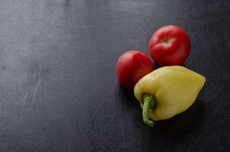 Sweet peppers and two ripe red tomatoes on a black table. Fresh organic vegetables. Farm products. Agroindustry.の写真素材