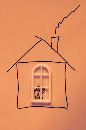 Child's drawing house on paper. White window is glued on top of the drawing. Domestic cat sit in the window. Concept of home comfort and love for animals. Toned photoの写真素材