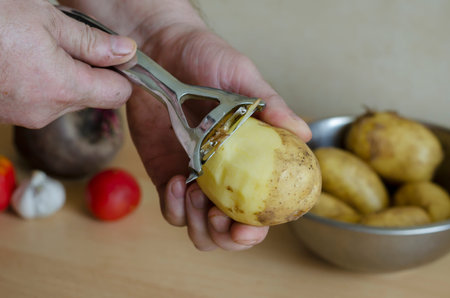 Middle-aged man peels raw potatoes. Caucasian man preparing food. Age 43-44. Life style. Side view. Selective focusの写真素材