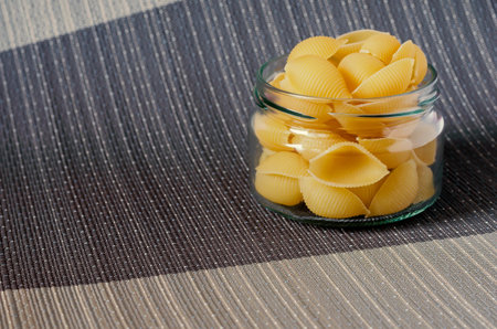 Raw Conchiglie Pasta in glass jar. Close-up of serving of uncooked pasta. Eco-friendly packaging for...