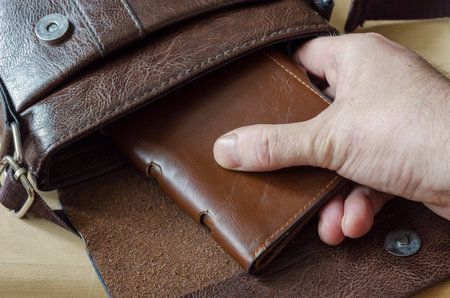 Male hand removes brown wallet from leather bag. Caucasian man takes out leather purse from an open...