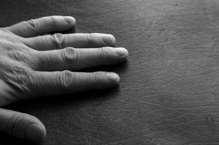 The palm of an adult Caucasian man lies on the table. His left wrinkled hand on a textured surface. A middle-aged man, 44-48 years old. A view from the side. Monochrome photoの写真素材