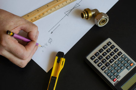 A male hand draws a diagram of home plumbing. Plumber makes the calculations. Caucasian man of...