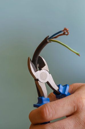 Hand cuts electric cable with copper wires with side cutters. Man's right hand with a black...