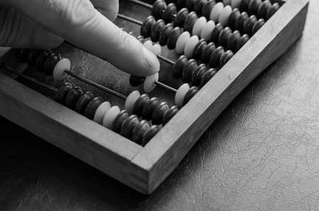 A middle-aged Caucasian man makes calculations on a wooden abacus. Close-up of a male hand. An obsolete tool for mathematical calculations. Monochromeの写真素材